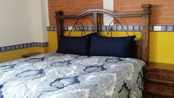 Una cama con colcha estampada, cabecero de madera y mesita de noche con cajones.