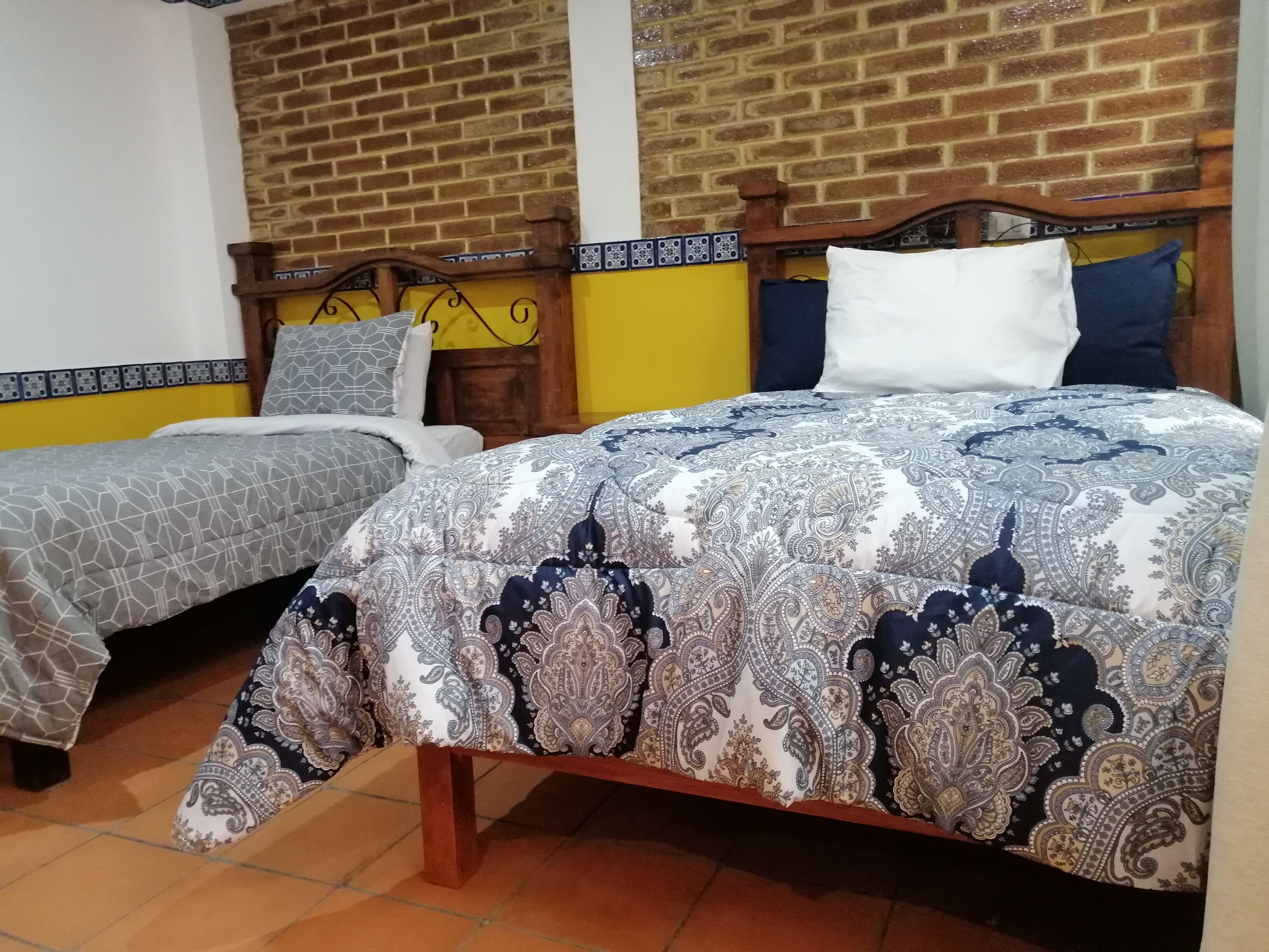 Una habitación con dos camas, cada una con ropa de cama estampada, una pared de ladrillo y una pared de acento amarilla.