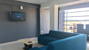 A modern living room with a large blue sectional sofa, a small coffee table, and a flat-screen TV mounted on the wall. - Hotel y Suites Axolotl (Chignahuapan)