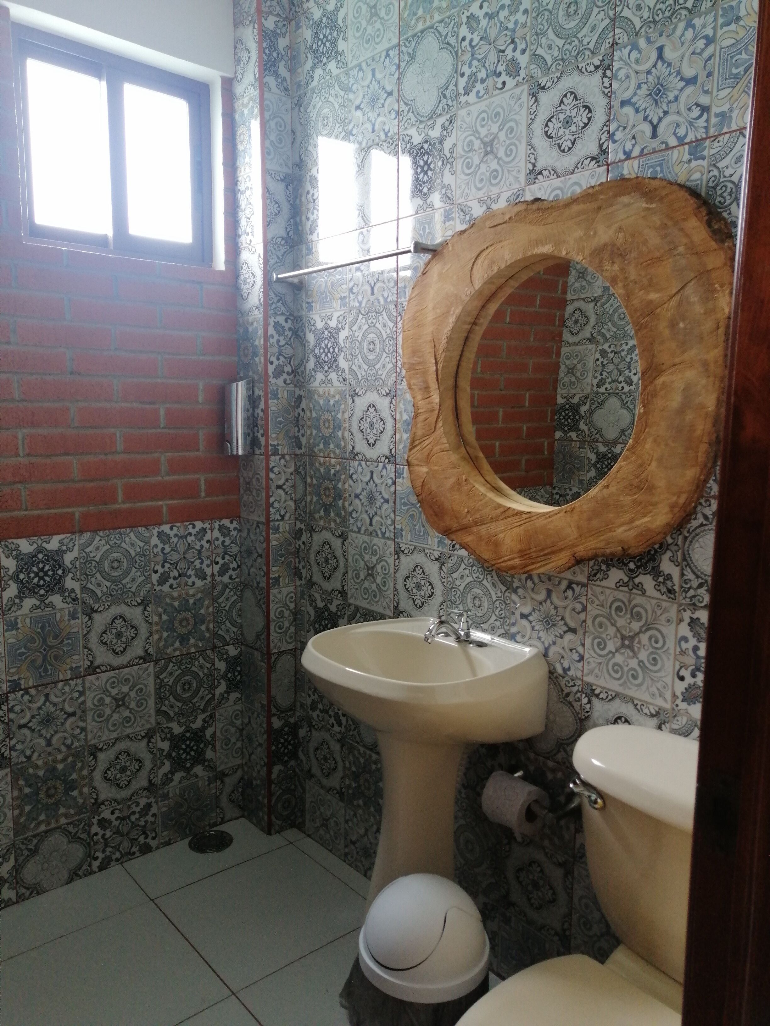 Une salle de bain avec des carreaux décorés, un miroir encadré en bois, un lavabo sur pied et des toilettes.