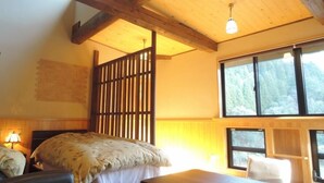 Quarto com cama, divisória de madeira, janela com vista para árvores e luminária.