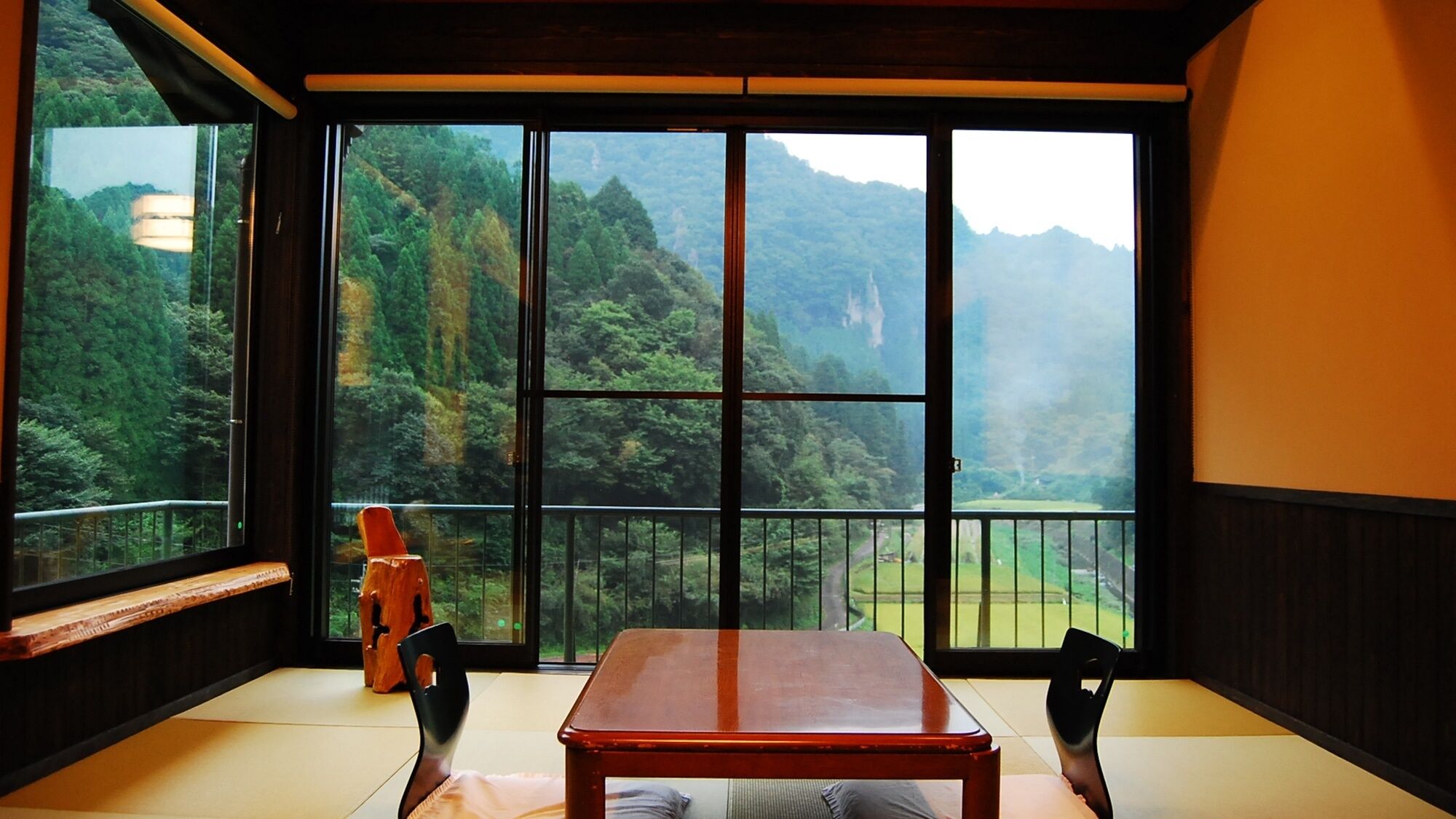 Una stanza con pavimento in tatami, un tavolo in legno e vista su un paesaggio montuoso attraverso ampie finestre.