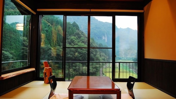 Quarto com piso de tatame, uma mesa de madeira baixa e vista para uma paisagem montanhosa através de grandes janelas.