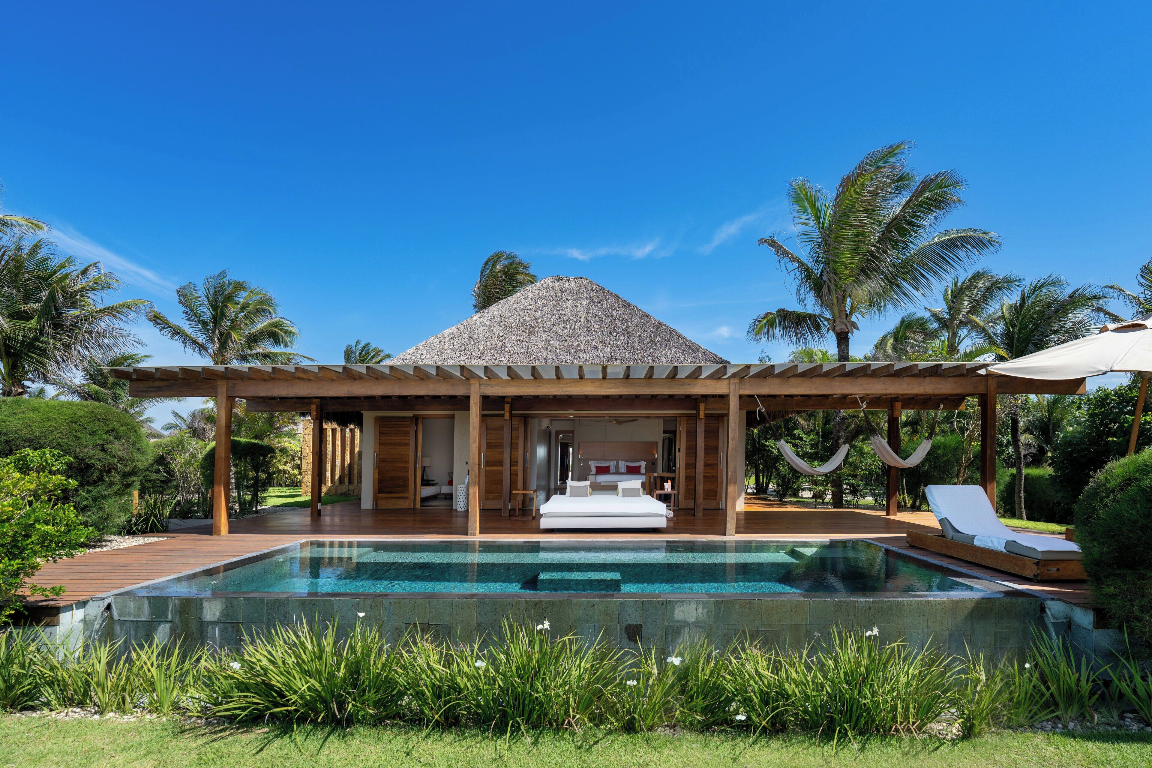 Uma área de piscina com um espaço de estar coberto, piscina e um edifício com telhado de palha.