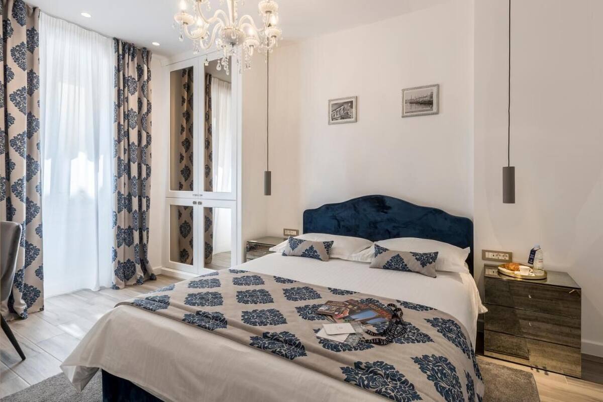 Ein Schlafzimmer mit einem großen Bett, einer Chandelier, einem Nachttisch und Blick ins Freie.