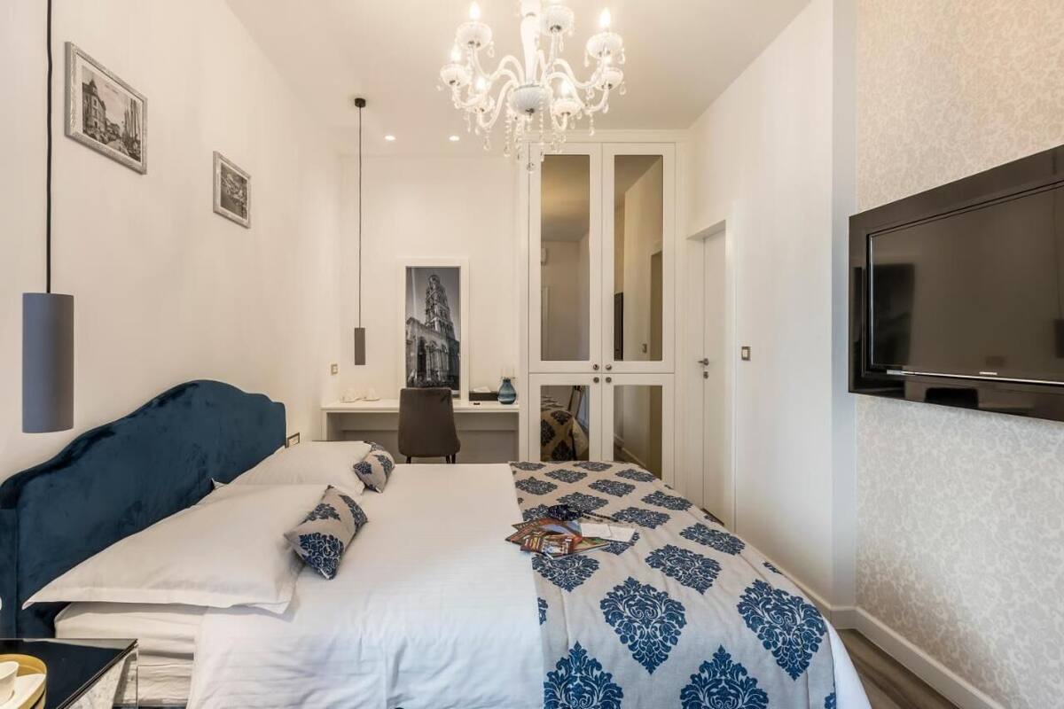 Ein Schlafzimmer mit Bett, Schreibtisch, Stuhl, Fernseher und einer Kristallleuchter.
