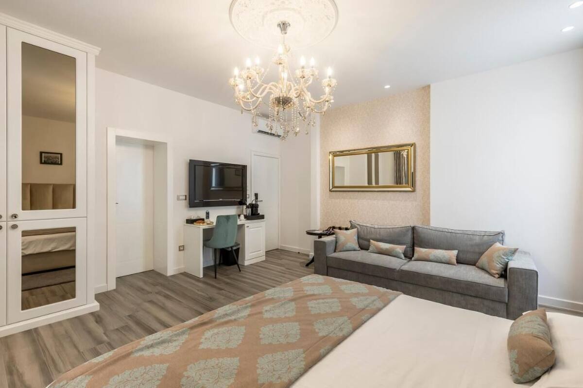 Ein Schlafzimmer mit einem Bett, einem Schreibtisch, einem Fernseher, einem Sofa und einem Kronleuchter.