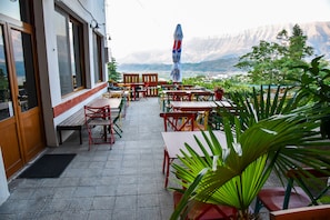 An outdoor seating area with tables and chairs, a view of mountains, and a potted plant. - Hotel Sofra (Gjirokastër)