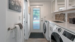 Un lavadero con lavadora y secadora de carga frontal, un lavabo y un perchero.