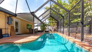 Una piscina con cerramiento de vidrio, rodeada por un patio con sillas y una mesa.