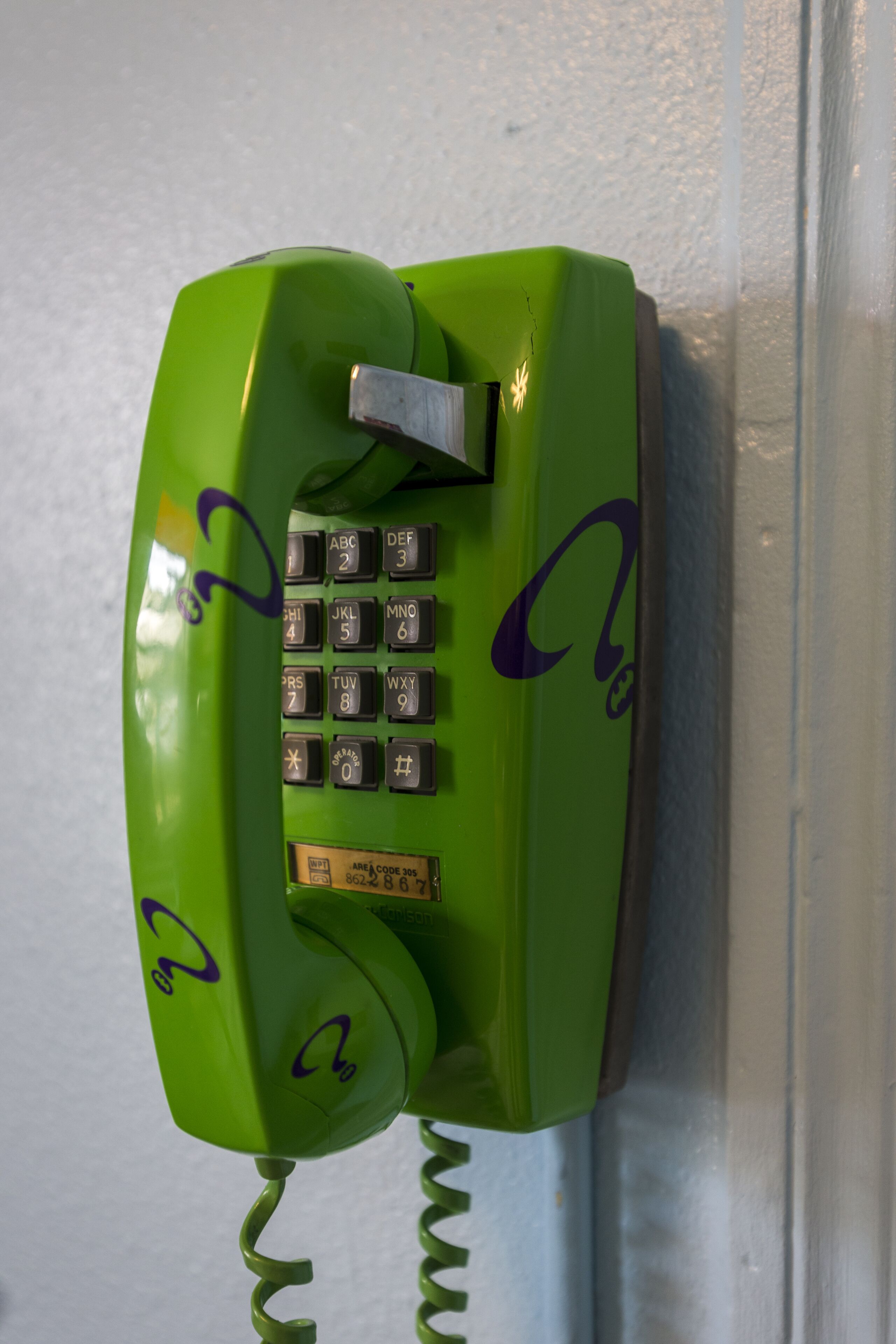 A green rotary dial telephone mounted on a wall.