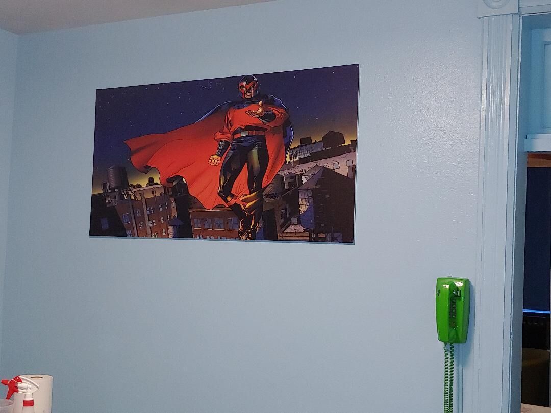 Une affiche de super-héros est accrochée à un mur, et un téléphone vert se trouve à côté.