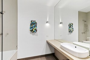 A modern bathroom with a large mirror, a white sink, and two towels hanging on the wall.