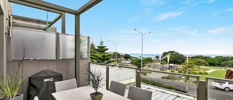 Ein Balkon mit Tisch, Stühlen, einem Grill und Blick auf die Straße und den Park.