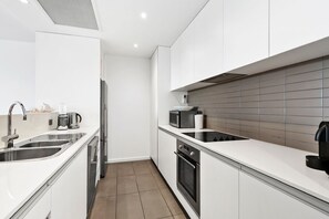 A modern kitchen with white cabinetry, stainless steel appliances, and a tiled backsplash. - Waterfront Two (Lorne)