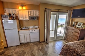 A compact kitchen with a refrigerator, stove, and microwave. There is a sliding glass door leading to a balcony with a view of the ocean. - Florence 1 608 (South Padre Island)