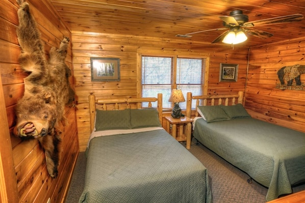 A cabin with two beds, a ceiling fan, and a bear head decoration.