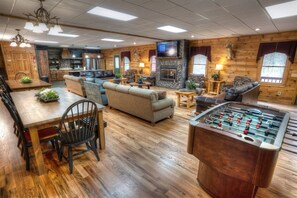 A cozy lodge with a dining area, sofas, a fireplace, and a foosball table.