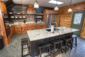 Eine Küche mit Holzausstattung, einer Arbeitsplatte aus Granit, einem Edelstahlkühlschrank und einer Bar mit Hockern.