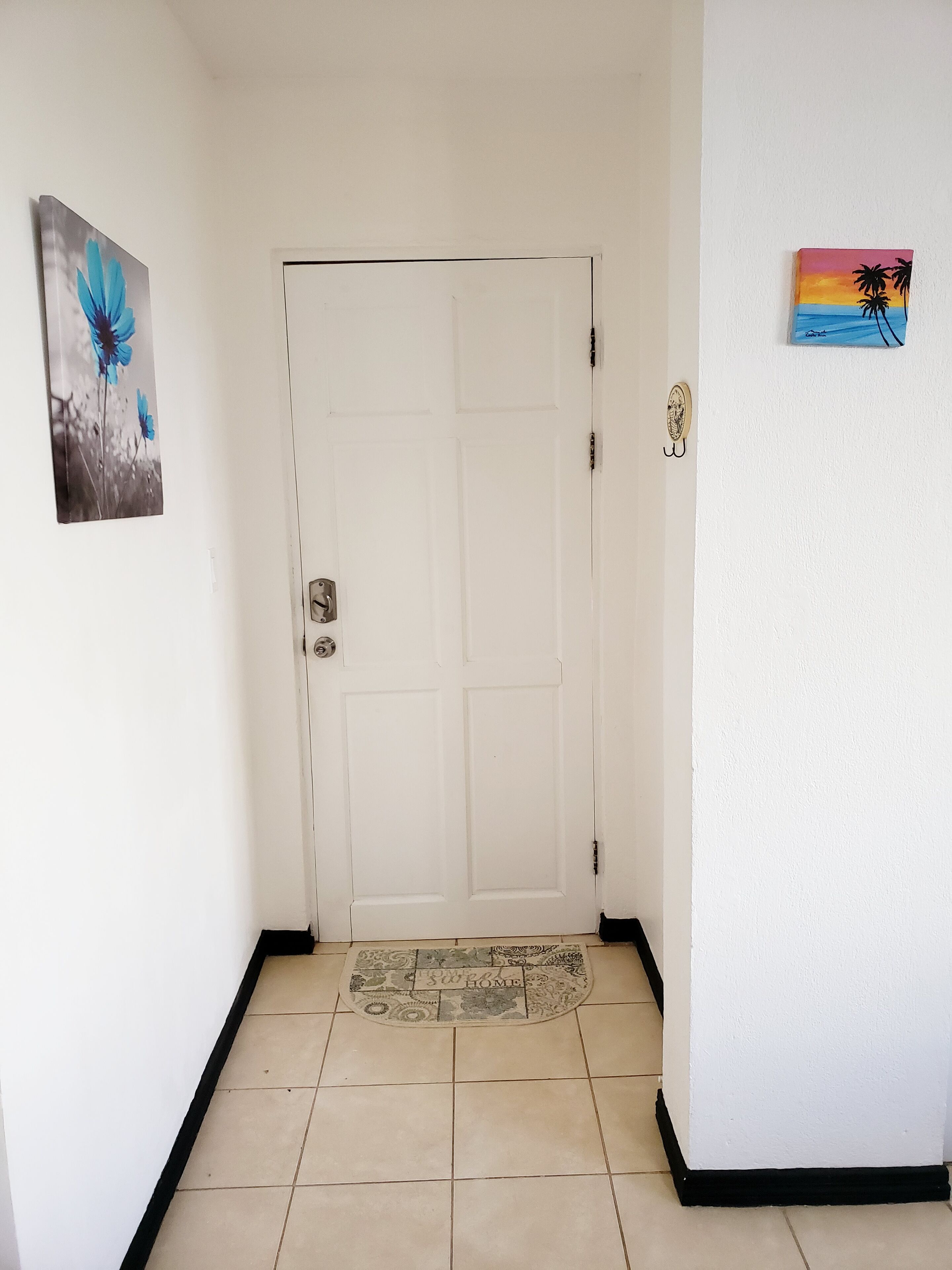 Un pasillo con una puerta blanca, un felpudo y dos cuadros colgados en la pared.