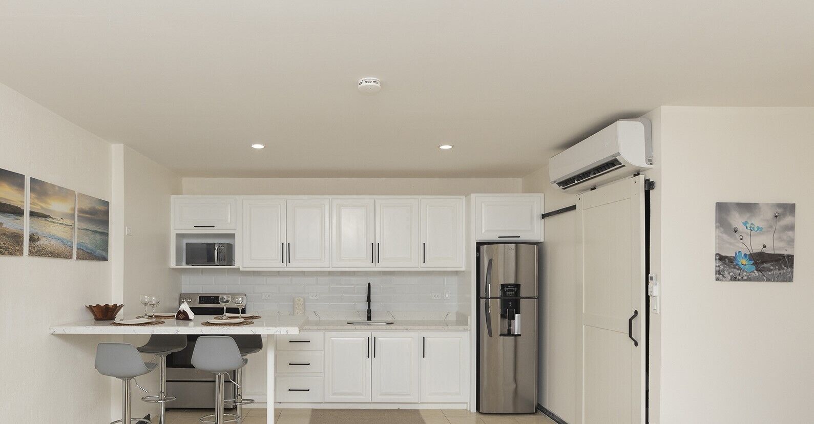 Una cocina moderna con armarios blancos, electrodomésticos de acero inoxidable y una zona de bar con taburetes.