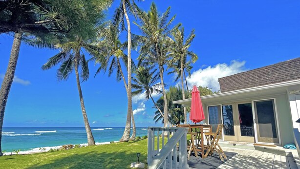 A beachfront property with a wooden deck, a red umbrella, and a view of the ocean.