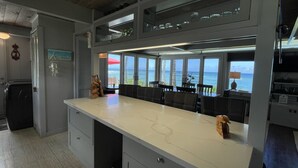 A kitchen with a large island, a dining area with a view of the ocean, and a refrigerator.