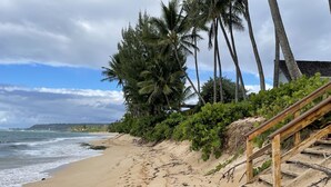 A beach with a wooden staircase leading down to the sand, palm trees, and a view of the ocean.