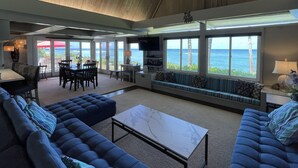 A spacious living area with a large window overlooking the ocean, a seating area with a sofa and a coffee table, and a dining area with a table and chairs.