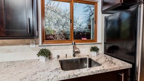 Eine Küche mit dunklen Holzschränken, einer Arbeitsplatte aus Granit, einer Spüle aus Edelstahl und einem Kühlschrank.
