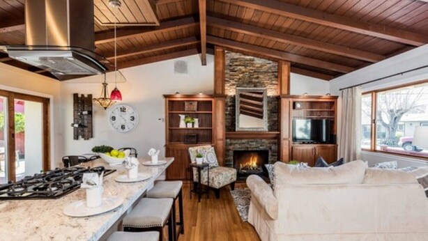 Eine moderne Küche mit Kamin aus Stein, Holzbalken und einer gemütlichen Sitzecke mit Sofa und Sesseln.