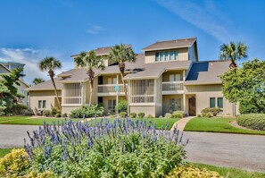 A multi-story residential building with balconies, a well-maintained lawn, and a variety of flowering plants.