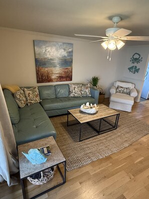 A living room with a sectional sofa, a coffee table, a side table, a ceiling fan, and a painting on the wall.