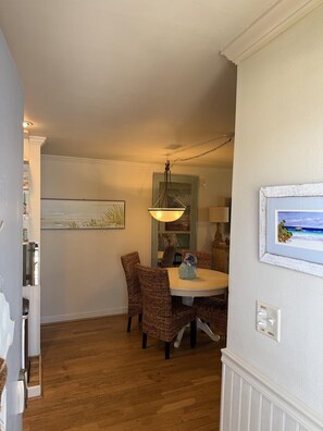 A dining area with a round table, wicker chairs, a hanging light fixture, and a framed picture on the wall.