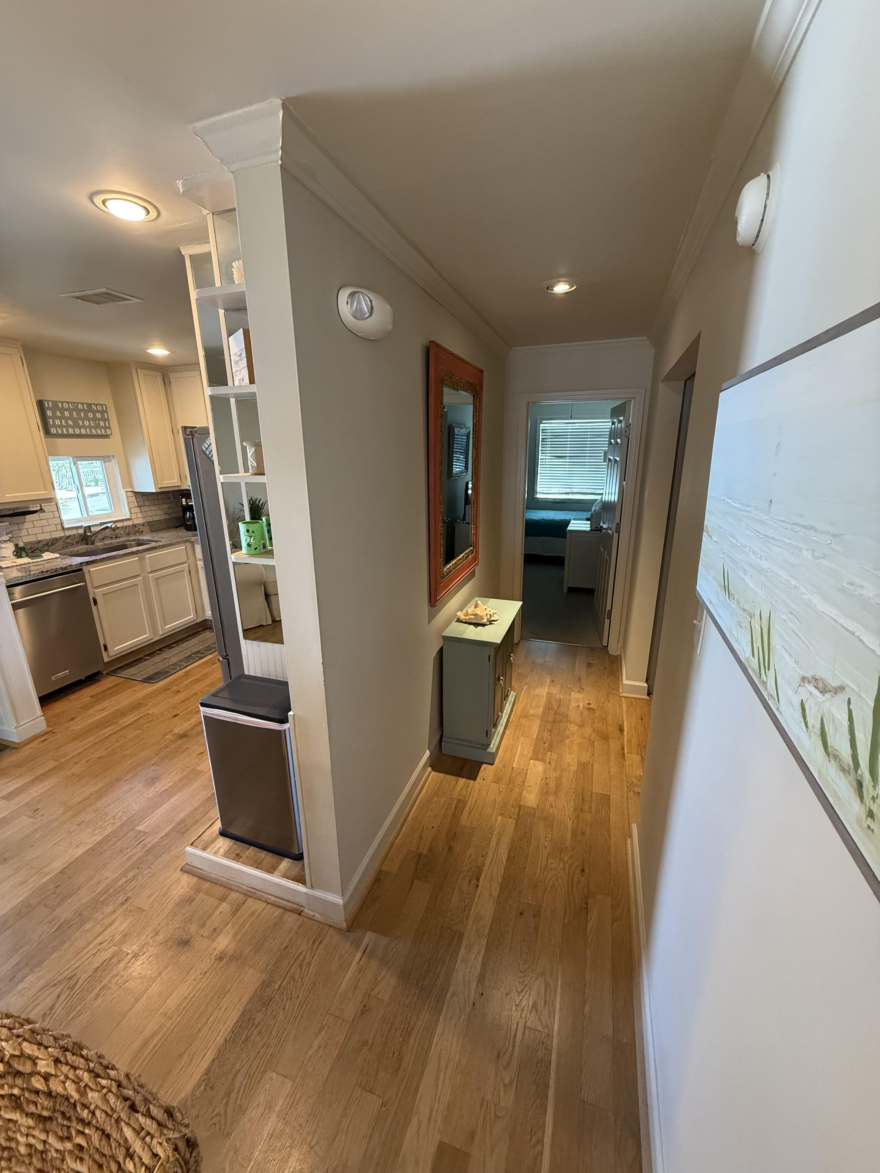 A modern kitchen with a built-in oven, a dining area with a bench, and a hallway leading to a bedroom.
