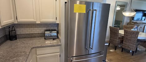 A kitchen with white cabinets, a stainless steel refrigerator, a granite countertop, and a dining area with wicker chairs.