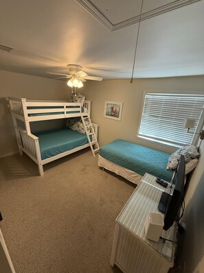 A bedroom with bunk beds, a ceiling fan, a window with blinds, and a desk with a television and remote controls. - C21 Sundown Riverside Condominiums (Pensacola)