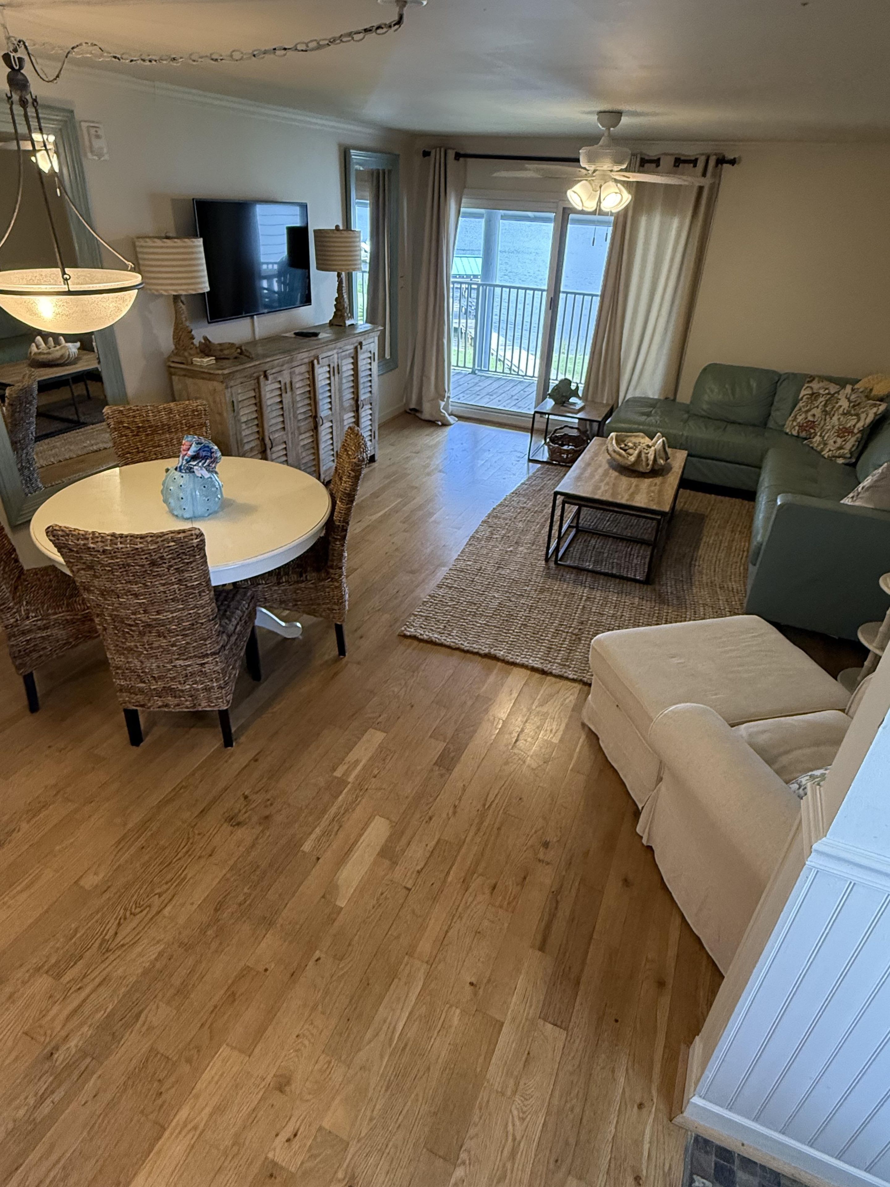 A living room with a dining area, a sofa, a television, and a balcony with curtains.