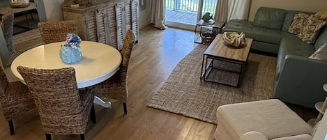 Een woonkamer met een eethoek, een bank, een televisie en een balkon met gordijnen.