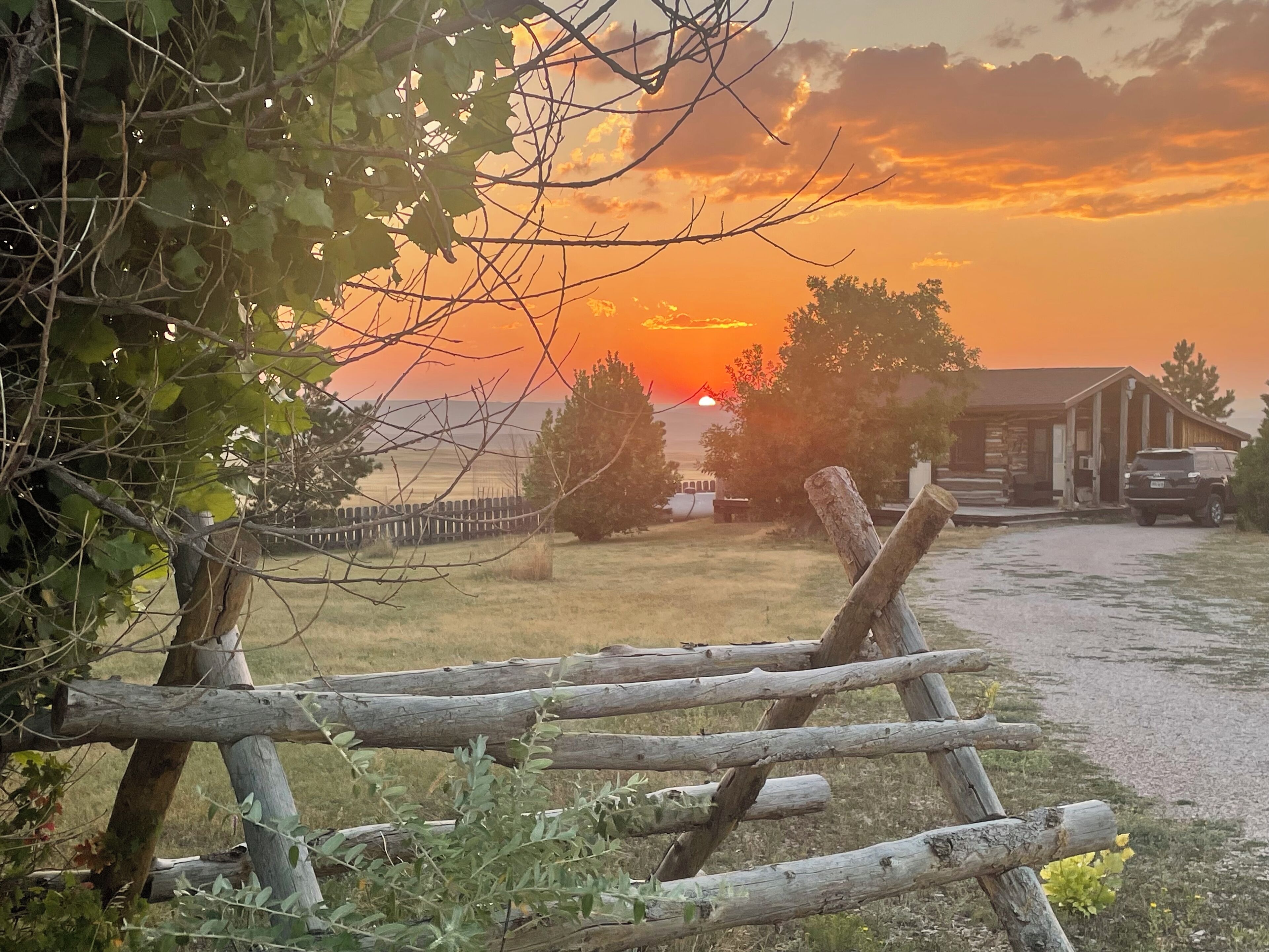 Ein rustikaler Holzzaun in ländlicher Umgebung, im Hintergrund ein Sonnenuntergang.