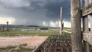 A rural landscape with a wooden fence, a metal gate, and a grassy field.