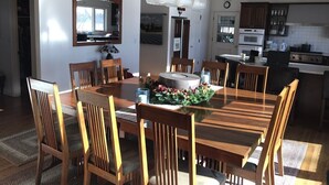 Un comedor con mesa y sillas de madera, una araña y una cocina al fondo.