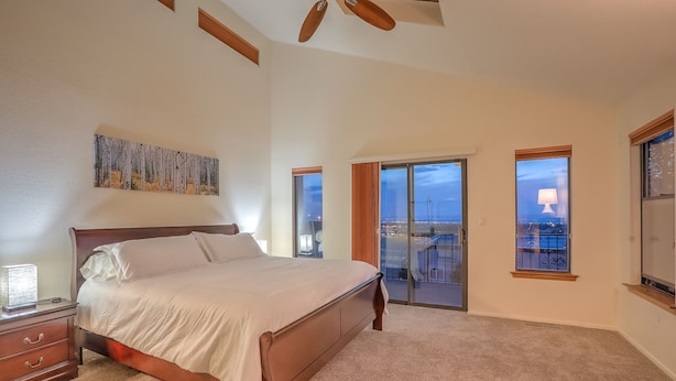 A bedroom with a large bed, a ceiling fan, a painting, and a balcony with a view. - Charming home in the Albuquerque foothills (Albuquerque)