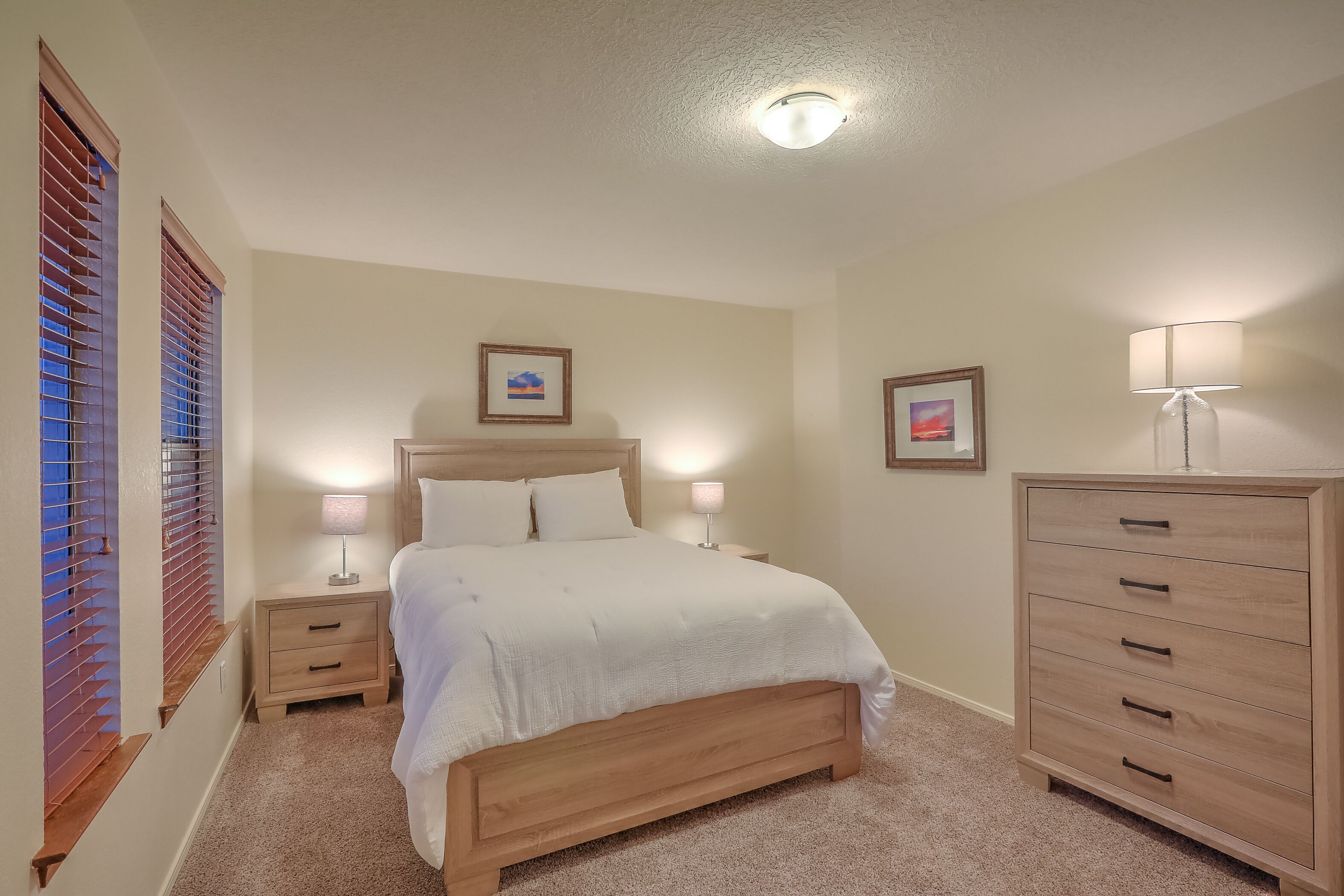 Een slaapkamer met een bed, nachtkastjes, een dressoir en wandlampen.