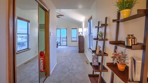 A hallway with a view to a balcony, a laundry basket, and shelves with plants and books. - Charming home in the Albuquerque foothills (Albuquerque)