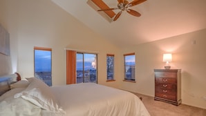 A bedroom with a large bed, a ceiling fan, a dresser, and multiple windows offering a city view. - Charming home in the Albuquerque foothills (Albuquerque)