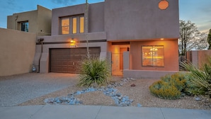 A modern two-story house with a garage, a well-maintained garden with rocks and plants, and a driveway. - Charming home in the Albuquerque foothills (Albuquerque)