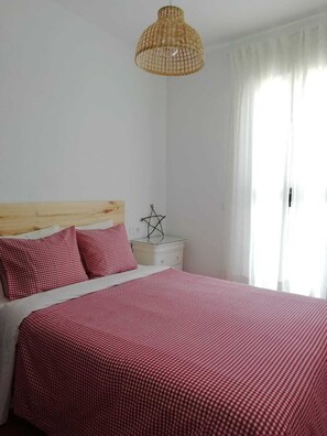 Ein Schlafzimmer mit einem Bett, einem Nachttisch, einer Pendelleuchte und einem Fenster mit Vorhängen.