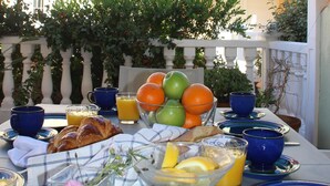 Ein Frühstückstisch gedeckt mit Croissants, Früchten und Orangensaft, mit Blick auf ein Gebäude und Grün im Hintergrund.