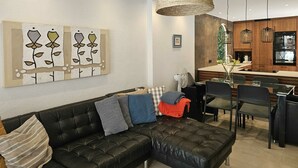 Ein modernes Wohnzimmer mit einer schwarzen Ledersofa, einem Essbereich mit Stühlen, einer Küche mit Holzschränken und einer hängenden Lampenschirm aus Rattan.